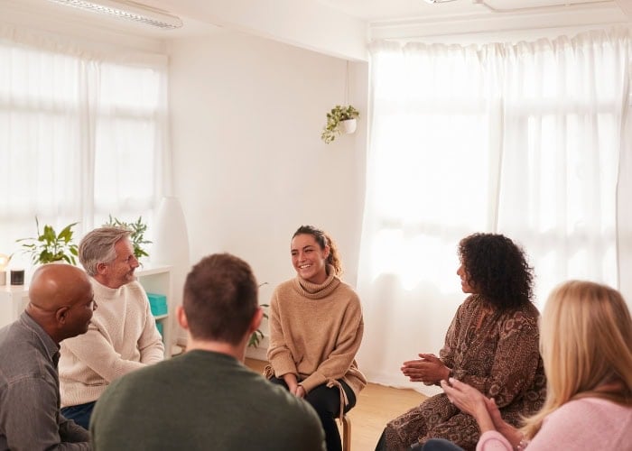 A support group of six adults is meeting in a bright room