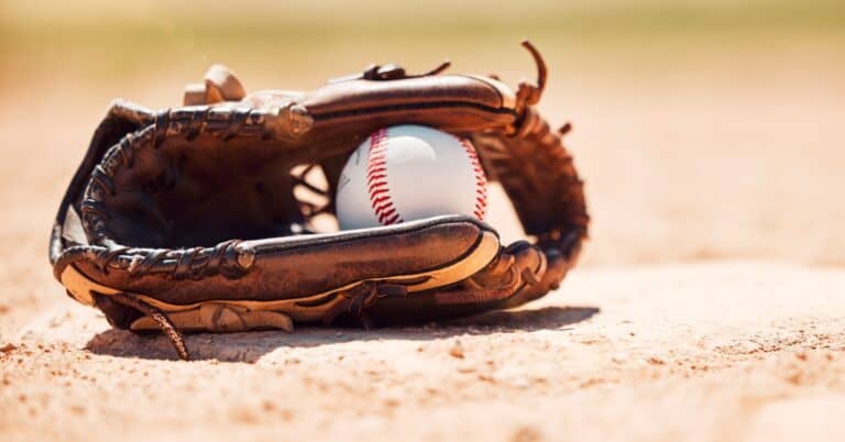 Softball in a glove laying on a diamond.