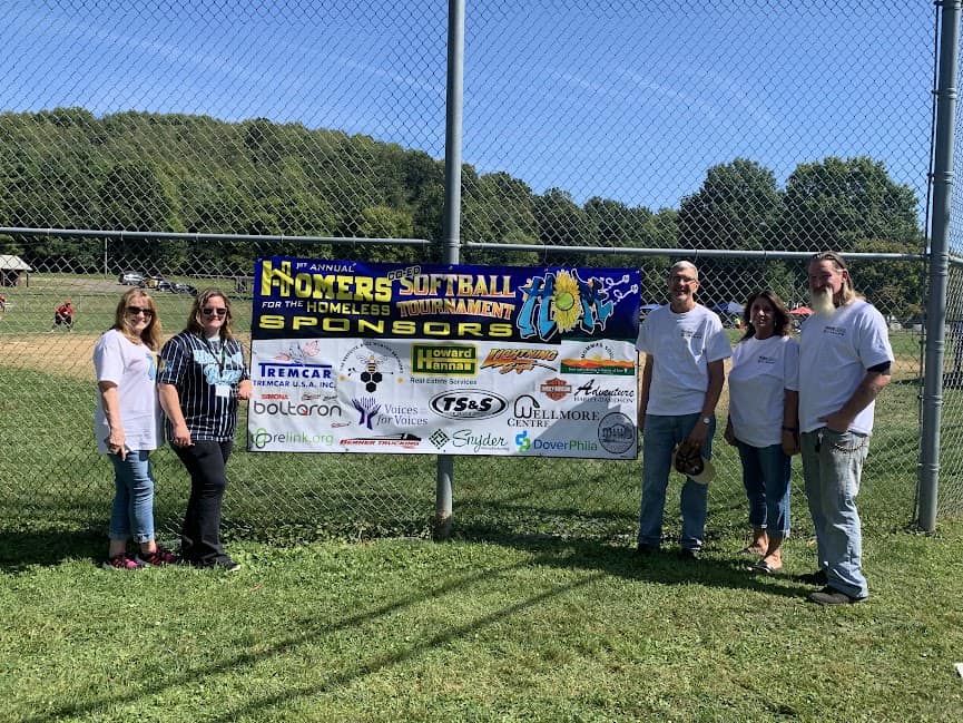 Sponsorship banner attached to a baseball field fence with 5 people standing next to it.